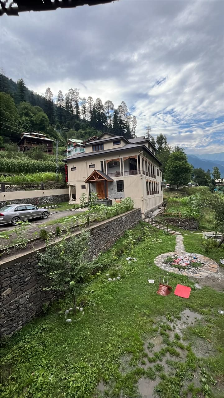 Apex Inn guest house above its stone-walled lawn with pine forest and Neelum Valley mountains behind