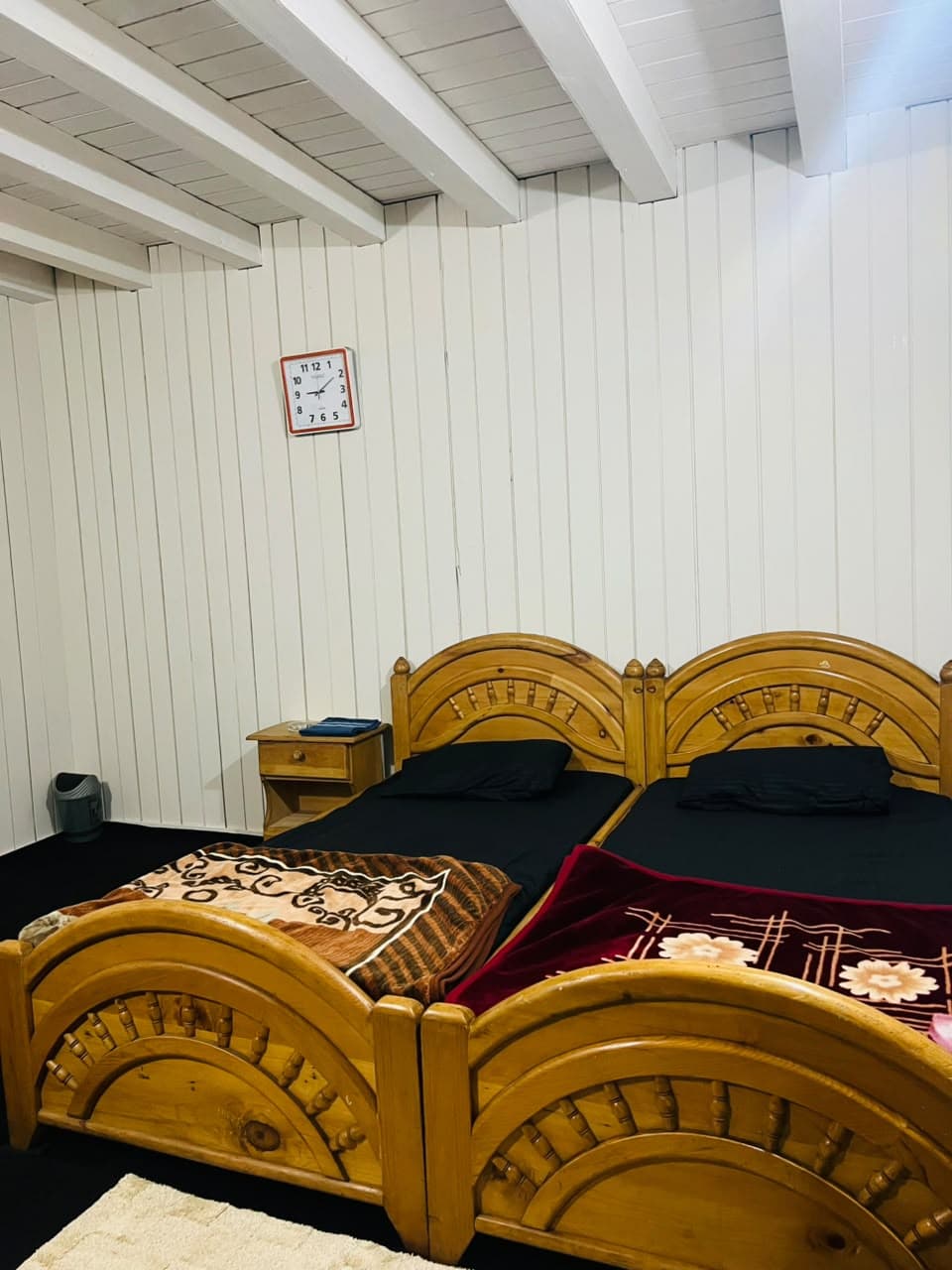 Wooden beds beside a bedside table and wall clock