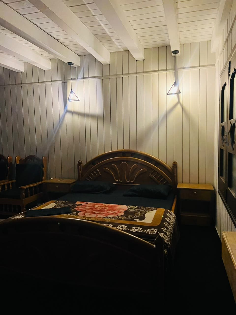 Double bed beside wooden armchairs under wall lights