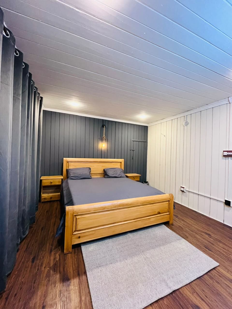 Guest room with a wooden double bed, grey feature wall and wood floor at Apex Inn