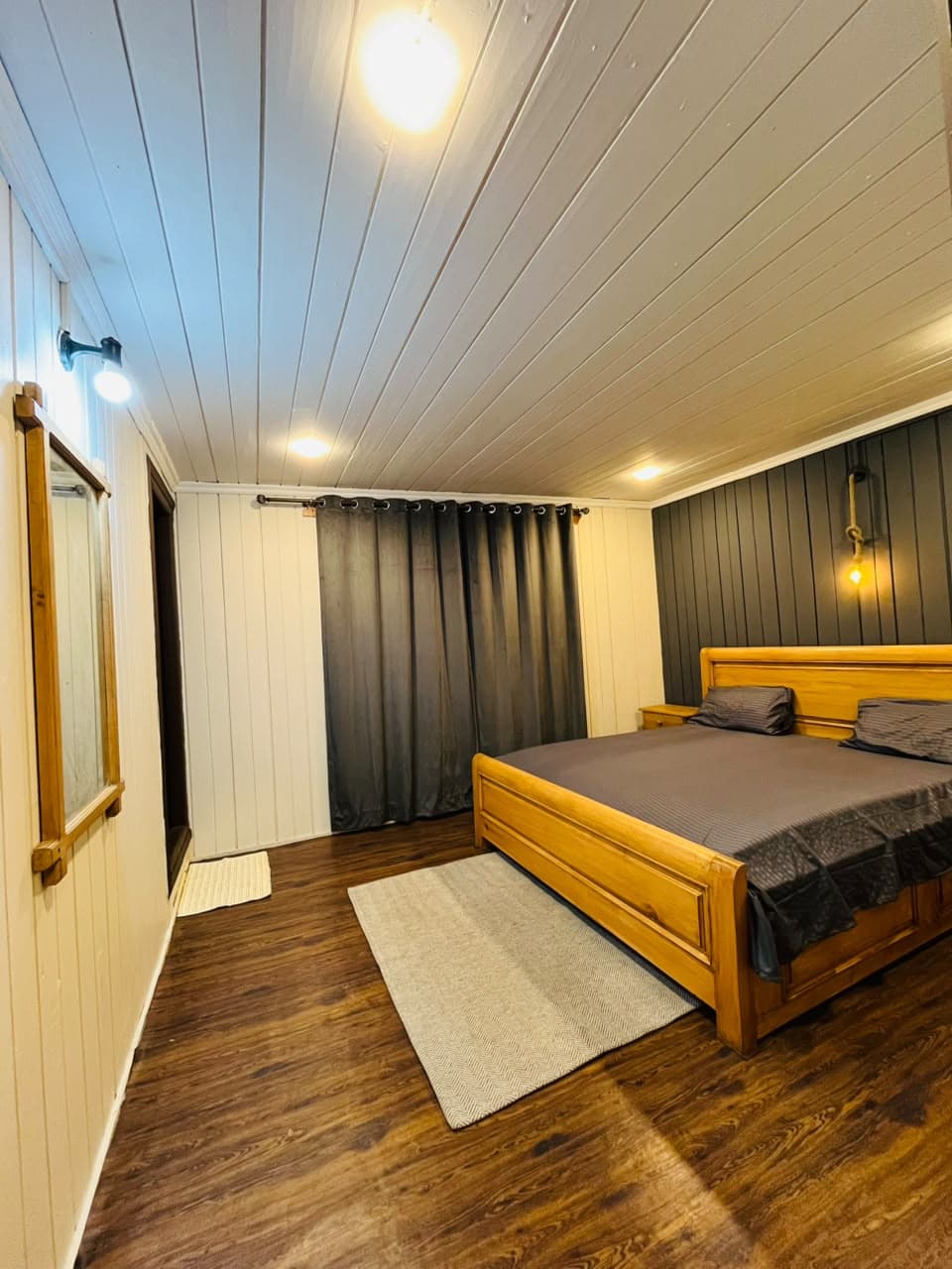 Guest room with grey curtains, wooden bed and wall mirror