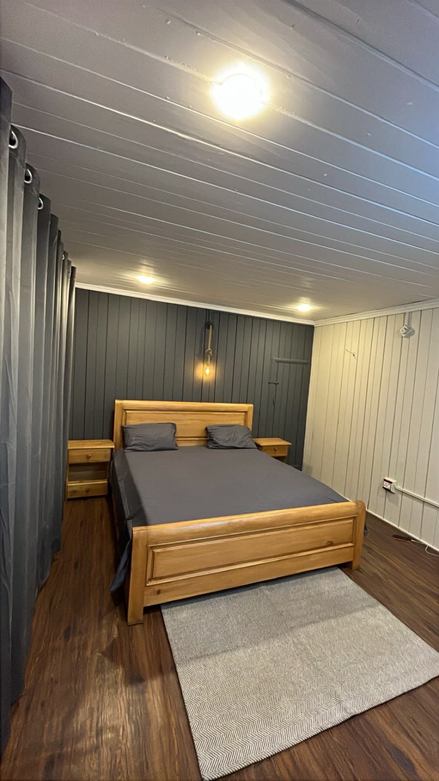 Guest room with a wooden bed, grey rug and curtained wall